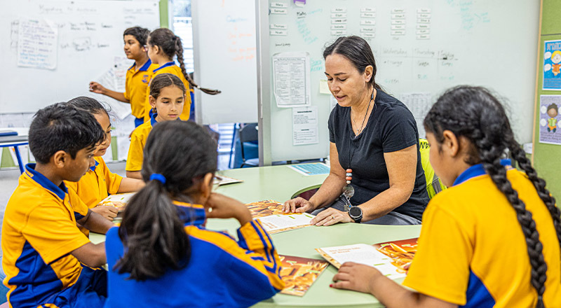 Teacher with students around a desk in the classroom at St Andrews Primary School Marayong
